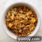 chex cereal, mini pretzels, and bugles in a large white bowl drizzled with spiced butter.