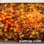 baked halloween chex mix on a baking sheet topped with pumpkin candies, candy corn, and reese's pieces.