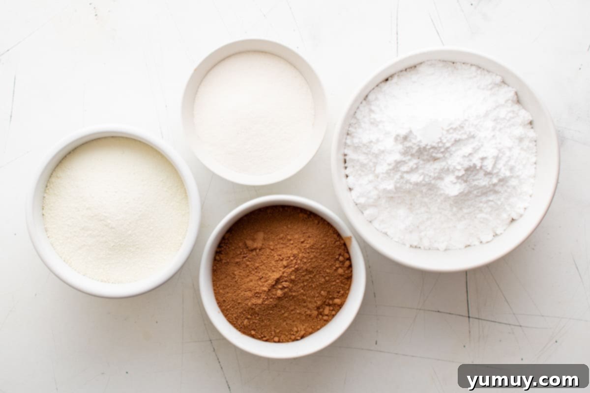 overhead view of individual ingredients for homemade hot chocolate mix in white bowls, neatly arranged on a counter.