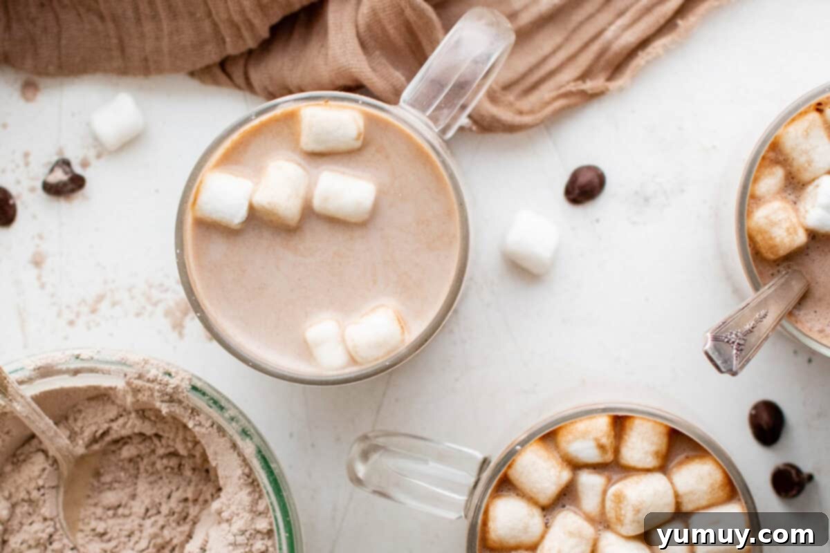 overhead view of a prepared homemade hot chocolate in a clear glass mug, topped generously with mini marshmallows, on a rustic surface.