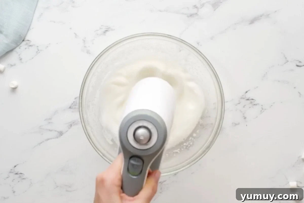 whipping egg whites with a hand mixer in a glass bowl.