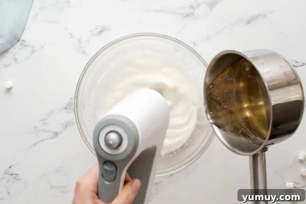 streaming sugar syrup into whipped egg whites in a glass bowl with a hand mixer.