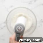 whipping egg whites with a hand mixer in a glass bowl.
