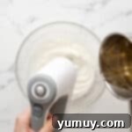 streaming sugar syrup into whipped egg whites in a glass bowl with a hand mixer.