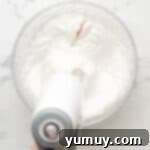 a splash of vanilla extract in a bowl of whipped egg whites and sugar with a hand mixer.