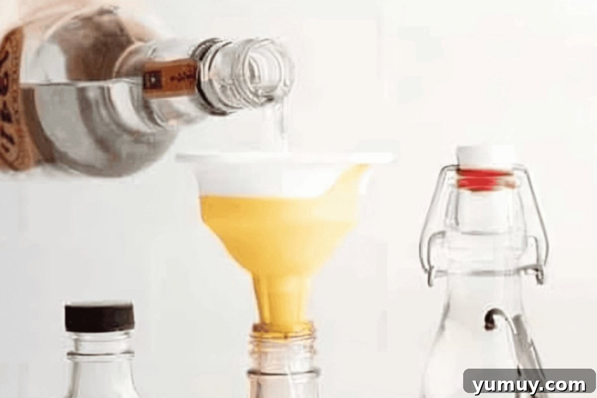 Pouring vodka through a funnel into a jar of vanilla beans, ensuring they are fully covered.