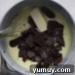 Butter, cream, and chunks of chocolate being whisked together in a saucepan.