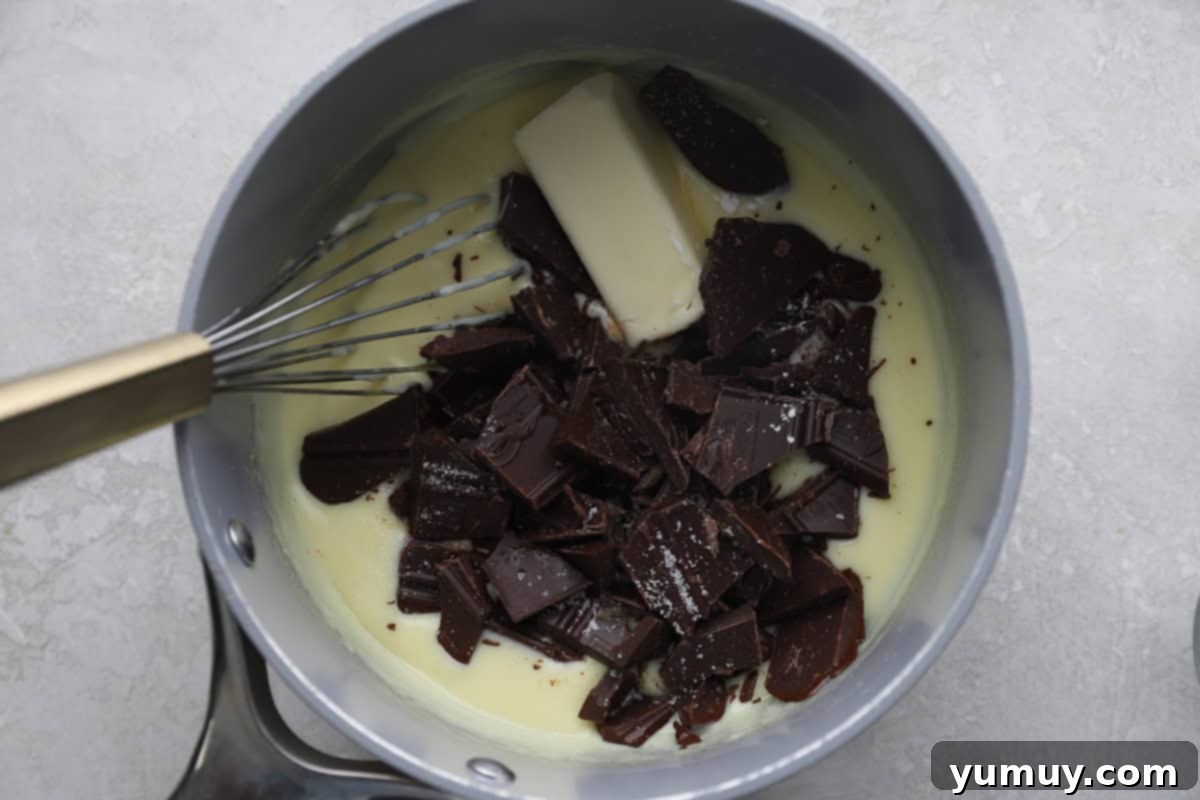 Butter, cream, and chunks of chocolate being whisked together in a saucepan.