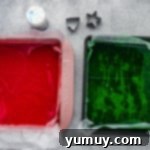 Two baking pans with parchment paper, one filled with red Jell-O gelatin, the other with green Jell-O gelatin, chilling.
