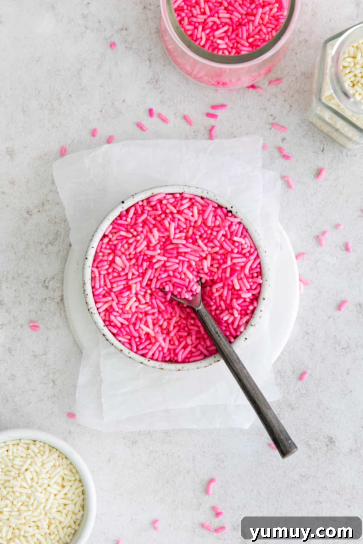 Crafting Custom Colored Sprinkles 2 A bowl brimming with an assortment of vibrant, homemade colored sprinkles, with a small spoon resting inside.