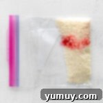 Crafting Custom Colored Sprinkles 5 A resealable bag containing white sprinkles and a drop of food dye, mid-mixing.