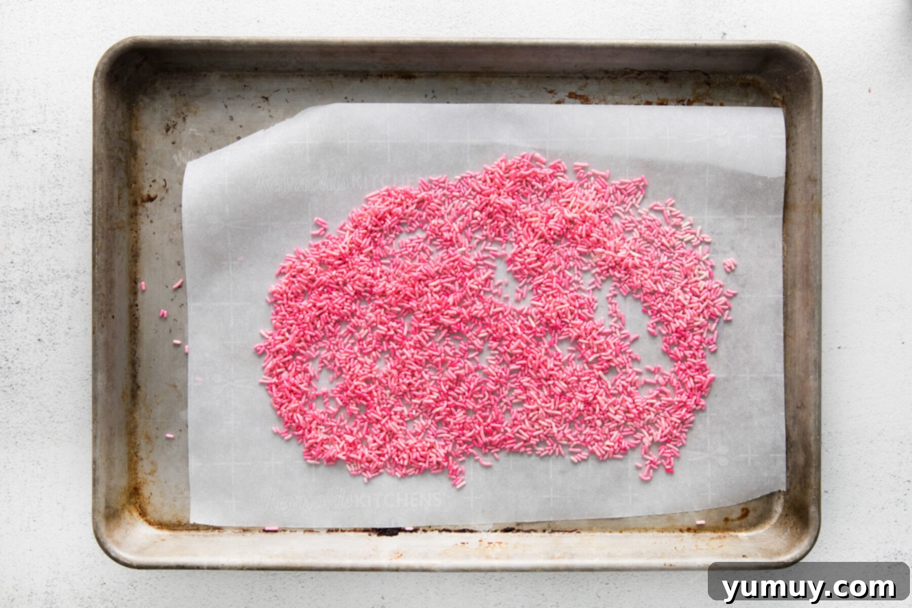 Crafting Custom Colored Sprinkles 9 Freshly dyed sprinkles spread evenly across parchment paper on a baking sheet, allowing them to air dry.