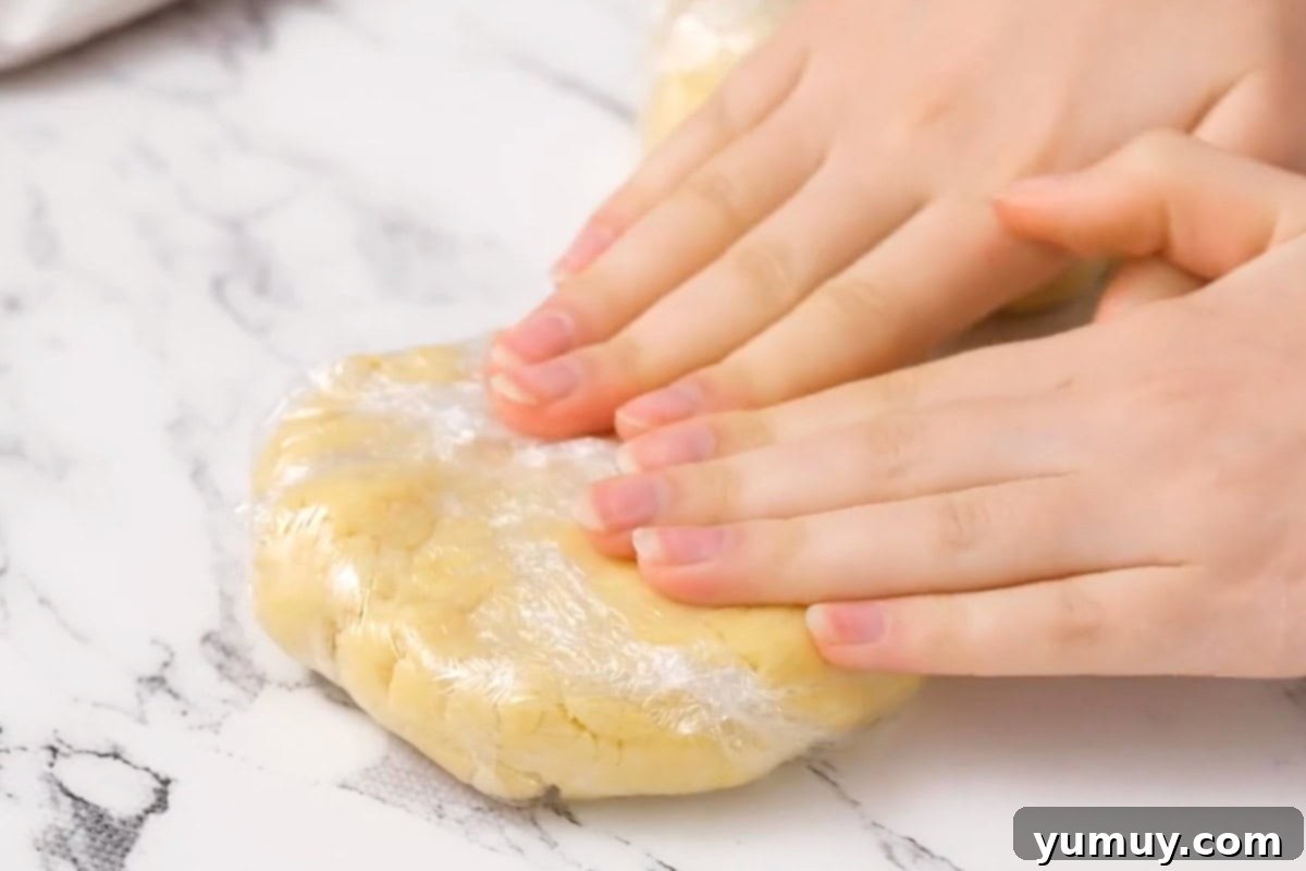 Pressing raw pie crust dough into a disc wrapped in plastic wrap.