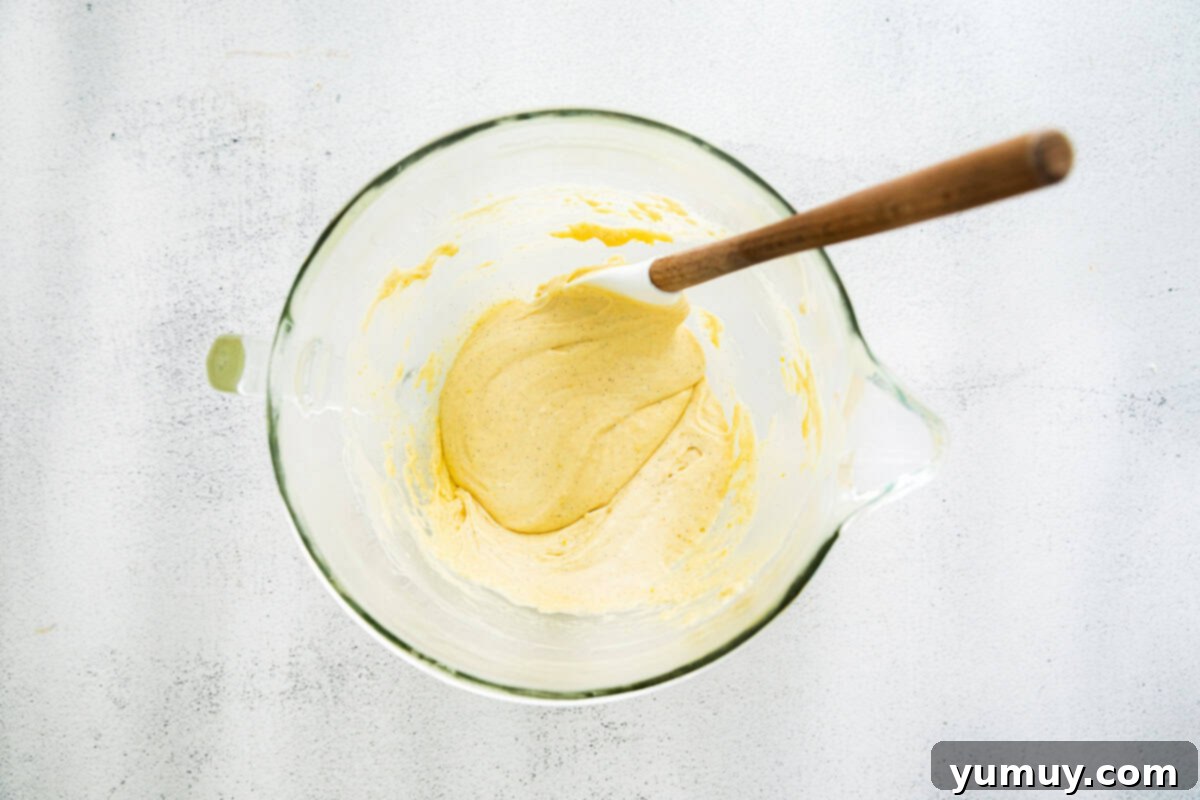 Delicate French Shell Cakes 13 thickened madeleine batter in a glass bowl with a rubber spatula.