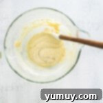 Delicate French Shell Cakes 6 folding madeleine batter in a glass bowl with a rubber spatula.