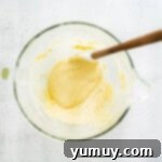 Delicate French Shell Cakes 7 thickened madeleine batter in a glass bowl with a rubber spatula.