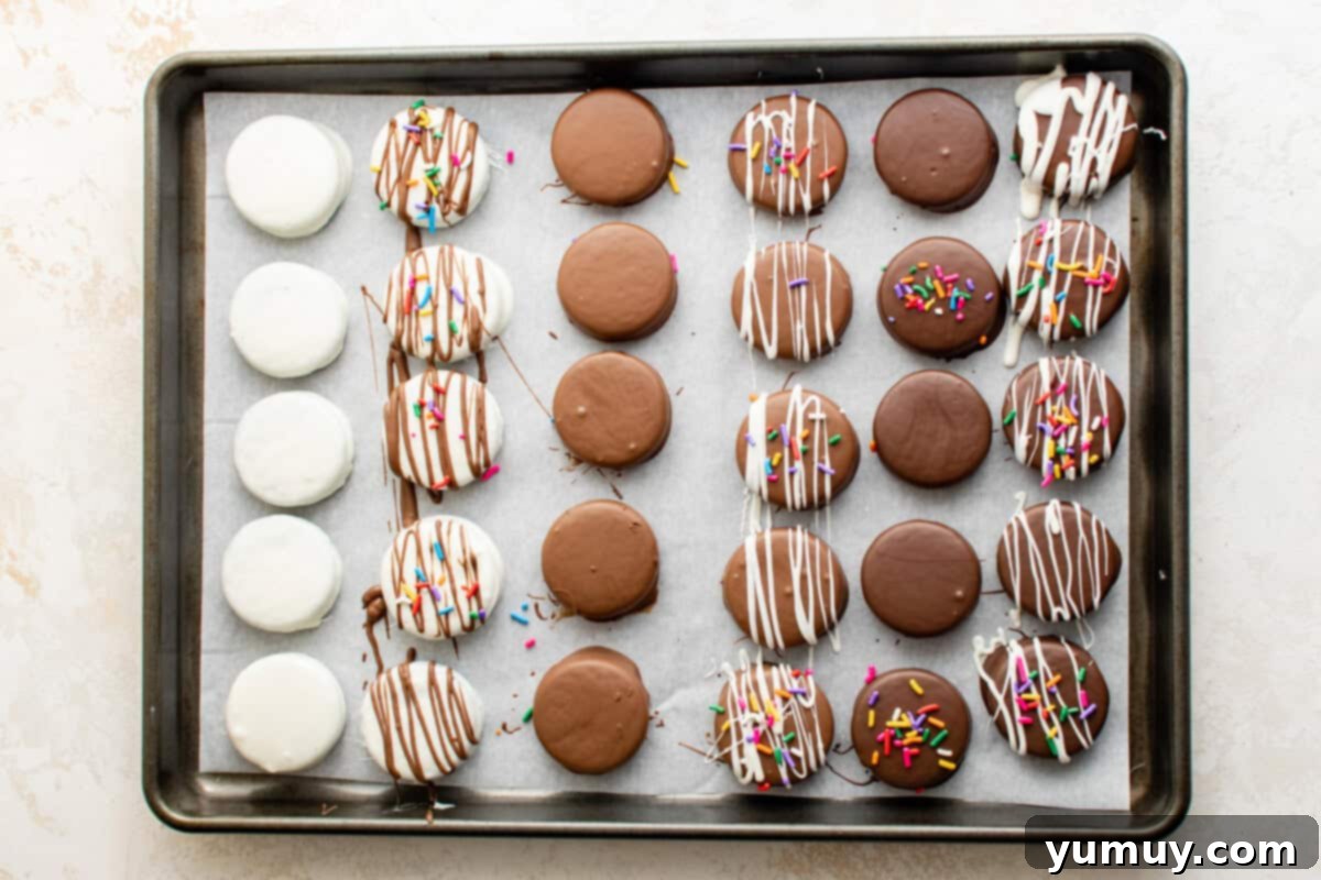 chocolate covered Oreos lined up on a baking tray; some are white chocolate, some are dark chocolate, some are milk chocolate; some are plain, some are drizzled with more chocolate, some have sprinkles