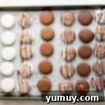 chocolate covered Oreos lined up on a baking tray; some are white chocolate, some are dark chocolate, some are milk chocolate; some are plain, some are drizzled with more chocolate, some have sprinkles