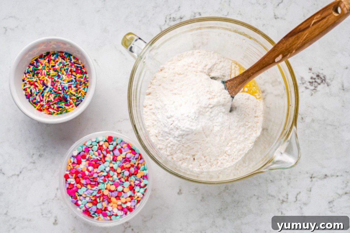 Cake Batter Confetti Cookies 11 Mixing together wet and dry ingredients in a large bowl to form cookie dough for confetti cake cookies.