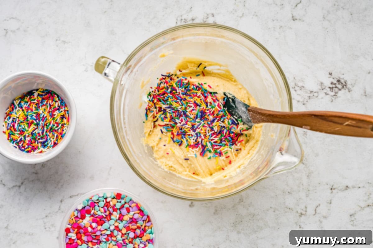 Cake Batter Confetti Cookies 12 Rainbow sprinkles being carefully folded into the cookie dough mixture in a mixing bowl.