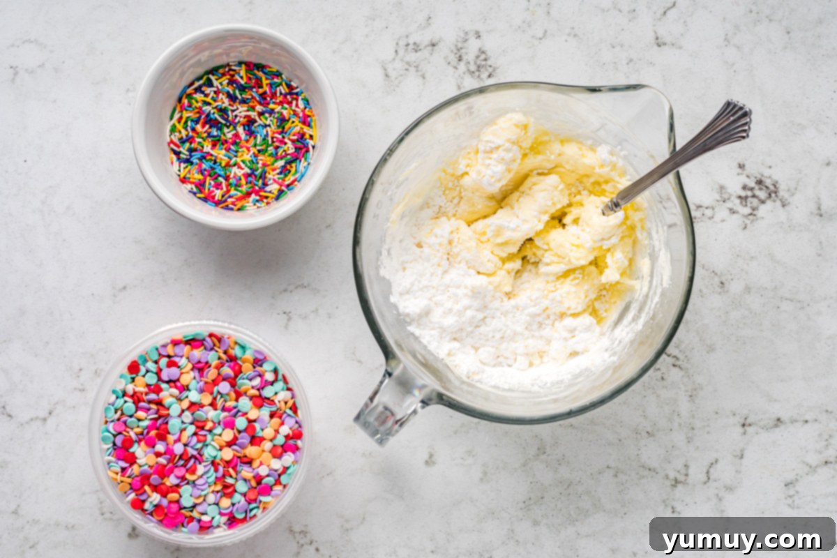 Cake Batter Confetti Cookies 15 A collection of frosting ingredients, including bowls of powdered sugar, butter, and cream cheese, on a kitchen counter.