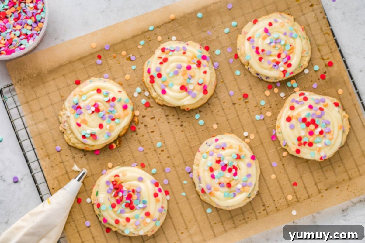 Cake Batter Confetti Cookies 16 A cooling rack laden with freshly frosted confetti cake cookies, each topped with a generous layer of creamy white frosting and vibrant rainbow sprinkles.
