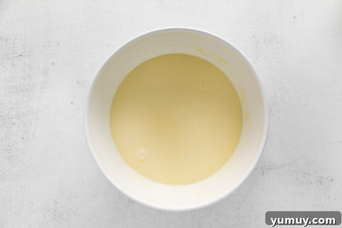 A white bowl with a yellow liquid in it, showing the combined milk, eggs, and vanilla with the previous wet ingredients.