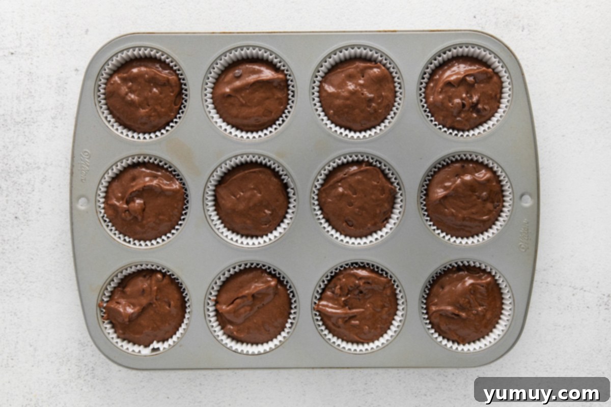 A muffin tin filled completely with chocolate batter, sprinkled with extra chocolate chips, ready for baking.