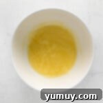 a bowl of yellow liquid on a white surface, representing whisked wet ingredients for muffins.