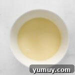 a white bowl with a yellow liquid in it, showing the combined milk, eggs, and vanilla.