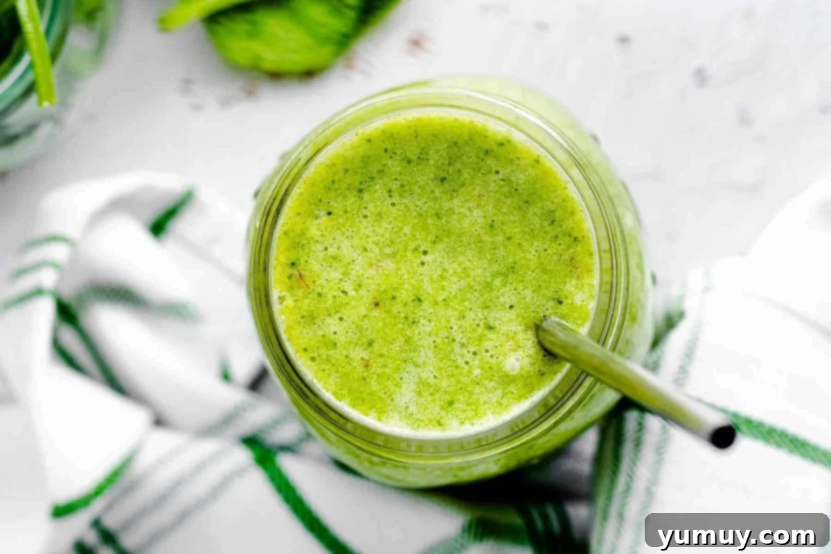 Overhead shot of an Island Green Smoothie in a mason jar with a metal straw, garnished with fresh fruit.