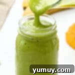 Pouring an island green tropical smoothie from a blender into a glass mason jar.