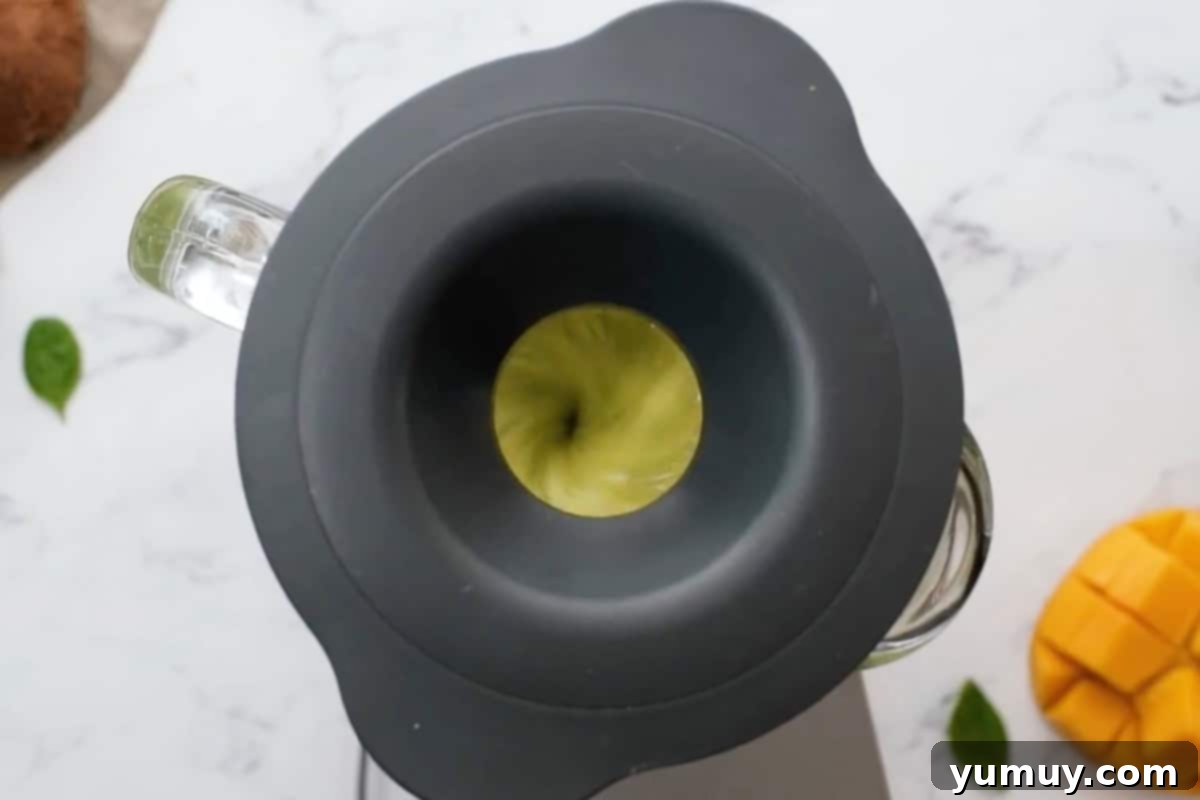 Blending an island green tropical smoothie in a high-powered blender with the lid securely on, creating a smooth green mixture.