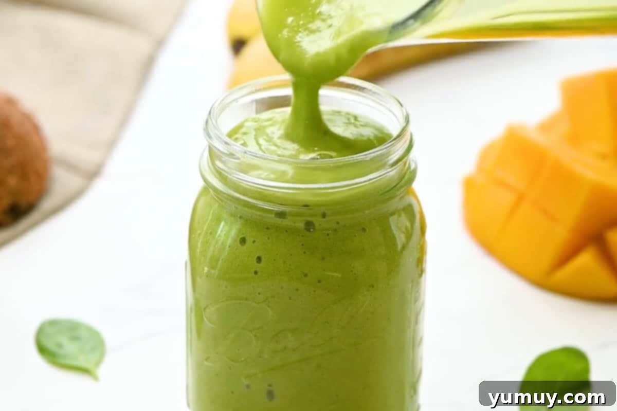 Pouring the freshly blended island green tropical smoothie from a blender into a clear glass mason jar, ready for serving.