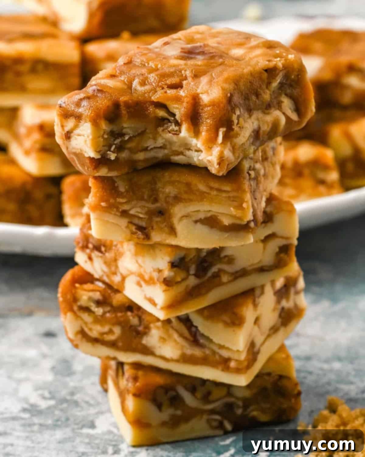 A bitten square of pralines and cream fudge on top of a stack of 3 pieces of fudge, showcasing the rich texture and pecan pieces.