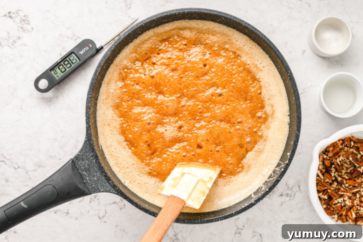 A frying pan containing the praline mixture actively boiling, with a spoon for occasional stirring.