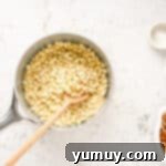 White chocolate chips melting in a saucepan with a wooden spoon stirring.
