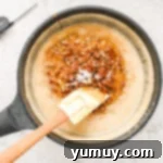 A frying pan with a wooden spatula, showing pecans and vanilla being stirred into the thickened praline mixture.
