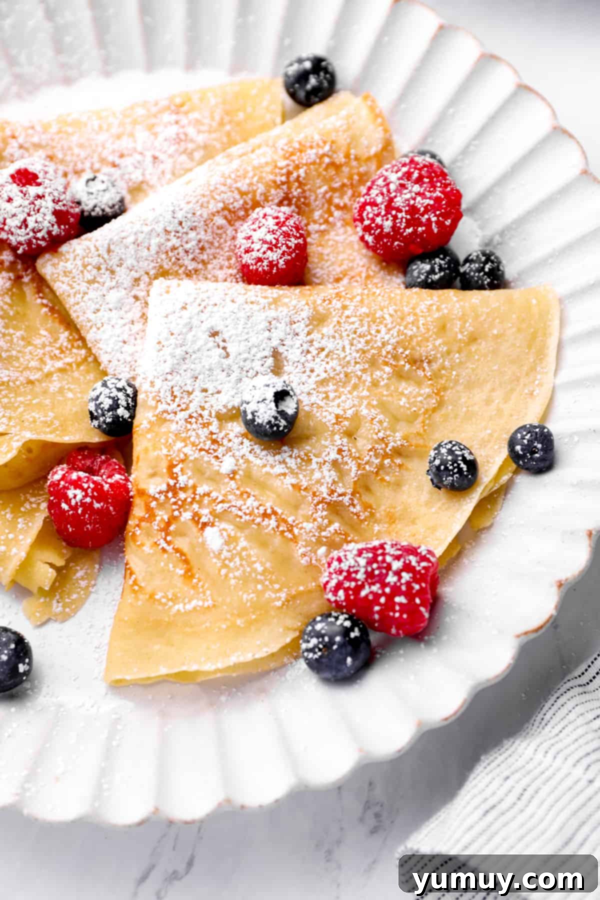 a plate of homemade crepes with berries and powdered sugar
