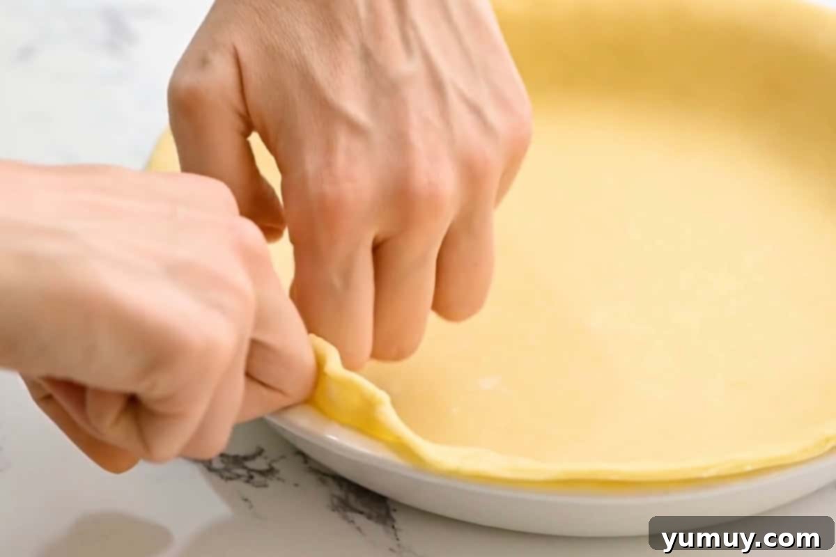 Close-up of hands expertly crimping the edges of a pie crust, preparing it for baking.