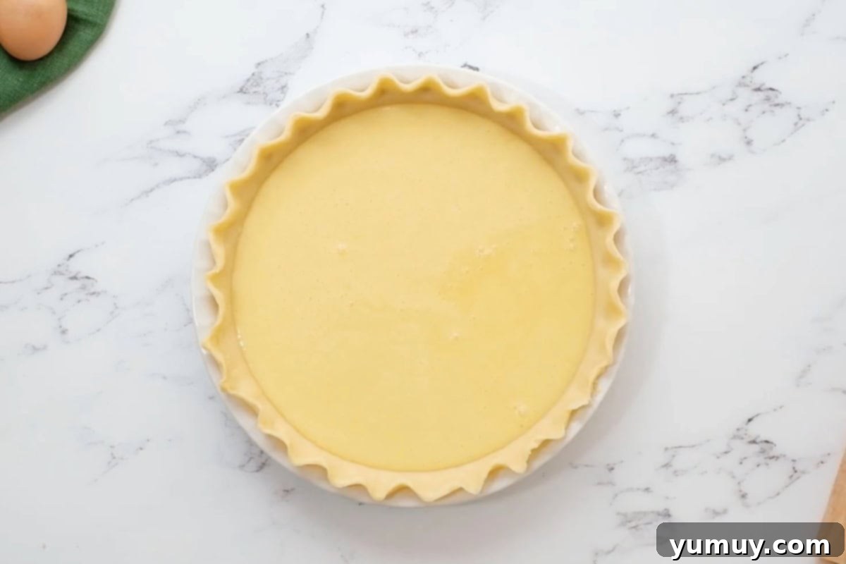 A crimped pie crust in a metal pie pan, filled to the brim with the smooth, uncooked buttermilk pie filling, ready for baking.