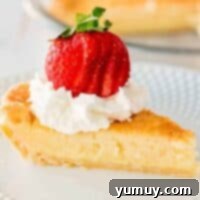 A slice of creamy buttermilk pie, topped with light whipped cream and a fresh strawberry, presented on a white plate.
