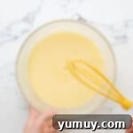Close-up of the smooth, pale yellow buttermilk pie filling in a glass bowl after all ingredients have been thoroughly whisked together.