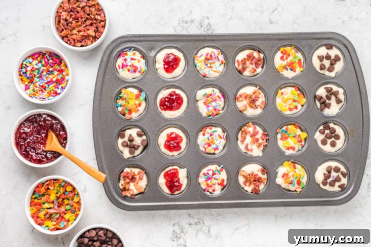Mini muffin tin with pancake batter, adorned with a variety of toppings like chocolate chips, cereal, and fruit.