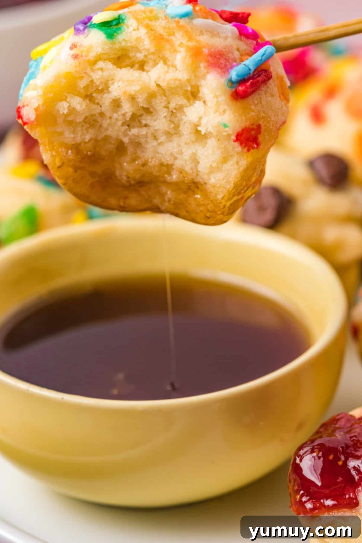 A mini pancake muffin being dipped into a small bowl of maple syrup, highlighting its golden exterior.