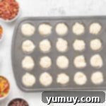 A mini muffin tin filled with pancake batter, with small bowls of various toppings placed nearby.