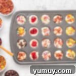 Close-up of a mini muffin tin with pancake batter, adorned with a variety of colorful and tasty toppings.