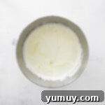 Fluffy cream cheese mixture with sugar and sour cream in a metal mixing bowl.