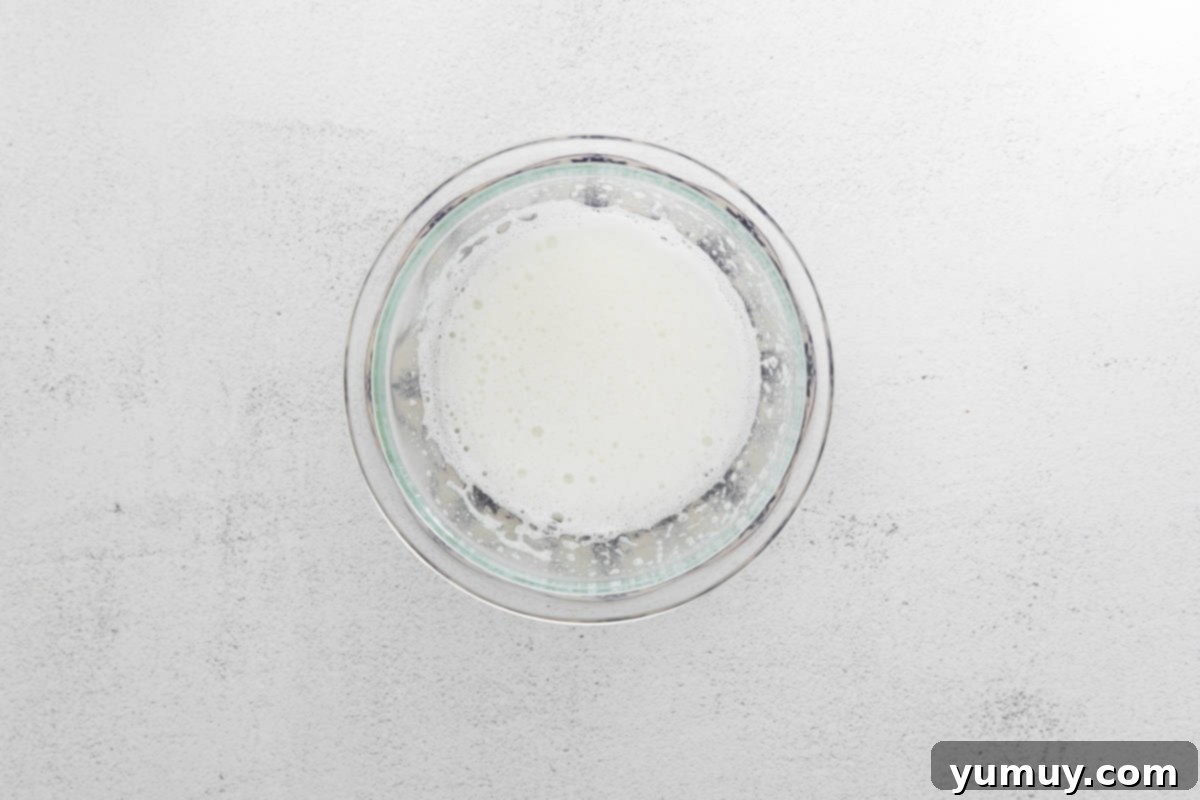 Egg whites and granulated sugar gently whisked in a glass bowl over a simmering saucepan, ensuring the sugar dissolves properly for the macaron meringue.