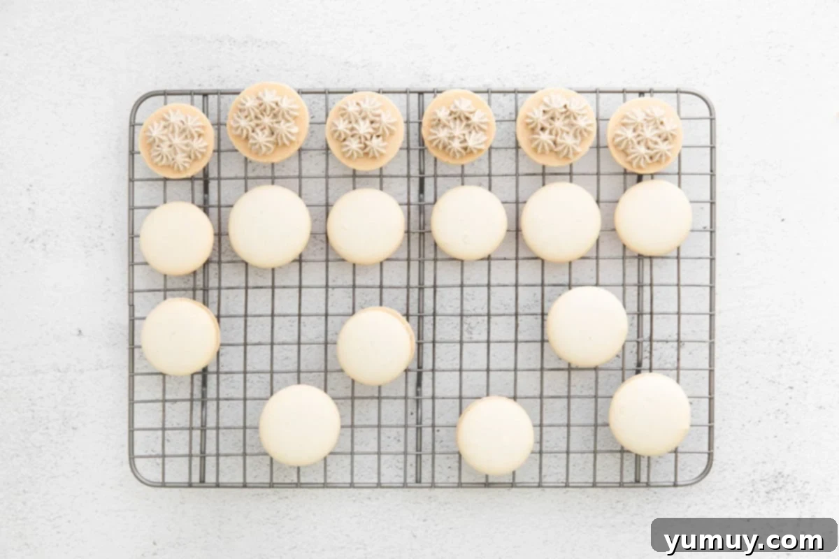 Macaron shells neatly arranged on a wire rack, being expertly filled with a creamy tiramisu frosting, showcasing the assembly process of the dessert.